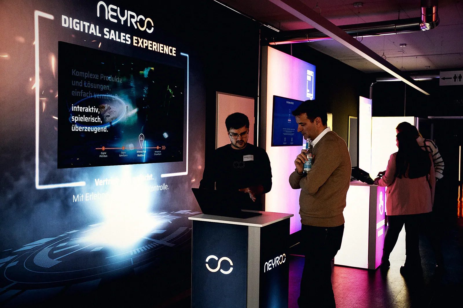Gespräch am digitalen Touchpoint: Neyroo-Vertrieb erklärt einem Besucher das Interactive WebDeck am Terminal